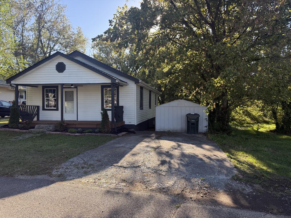 White single-story house with dark trim, a covered porch, and a detached shed beside the driveway.
