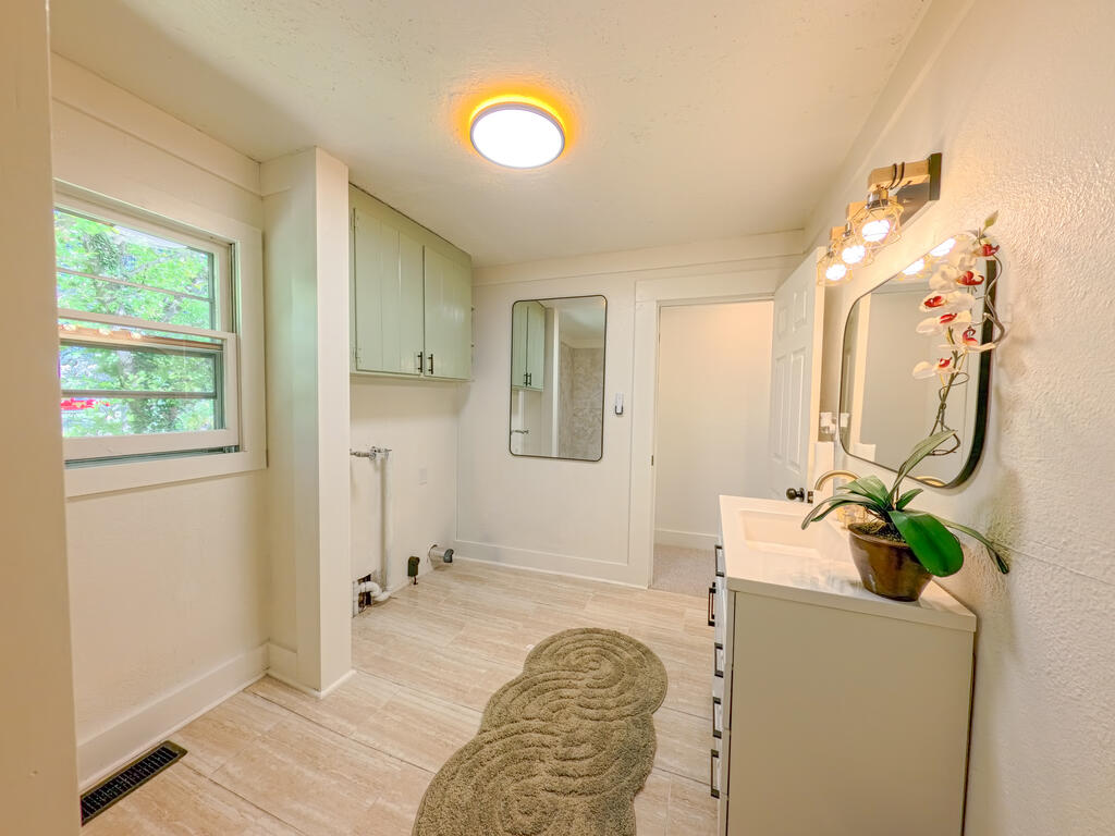 Bathroom with a long vanity, illuminated mirror, potted orchid, and window overlooking green foliage.