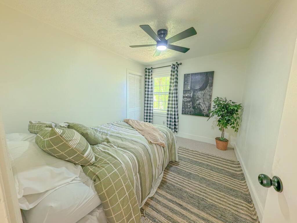 Bedroom with green-and-white striped bedding, checked curtains, and a ceiling fan.
