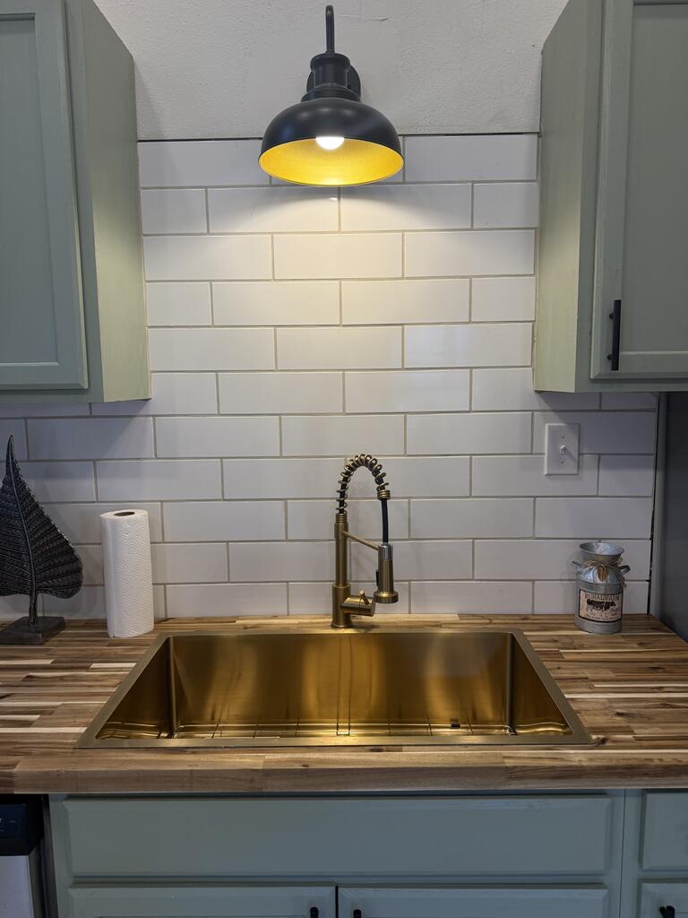 Kitchen sink with brass basin and faucet beneath white subway tile.