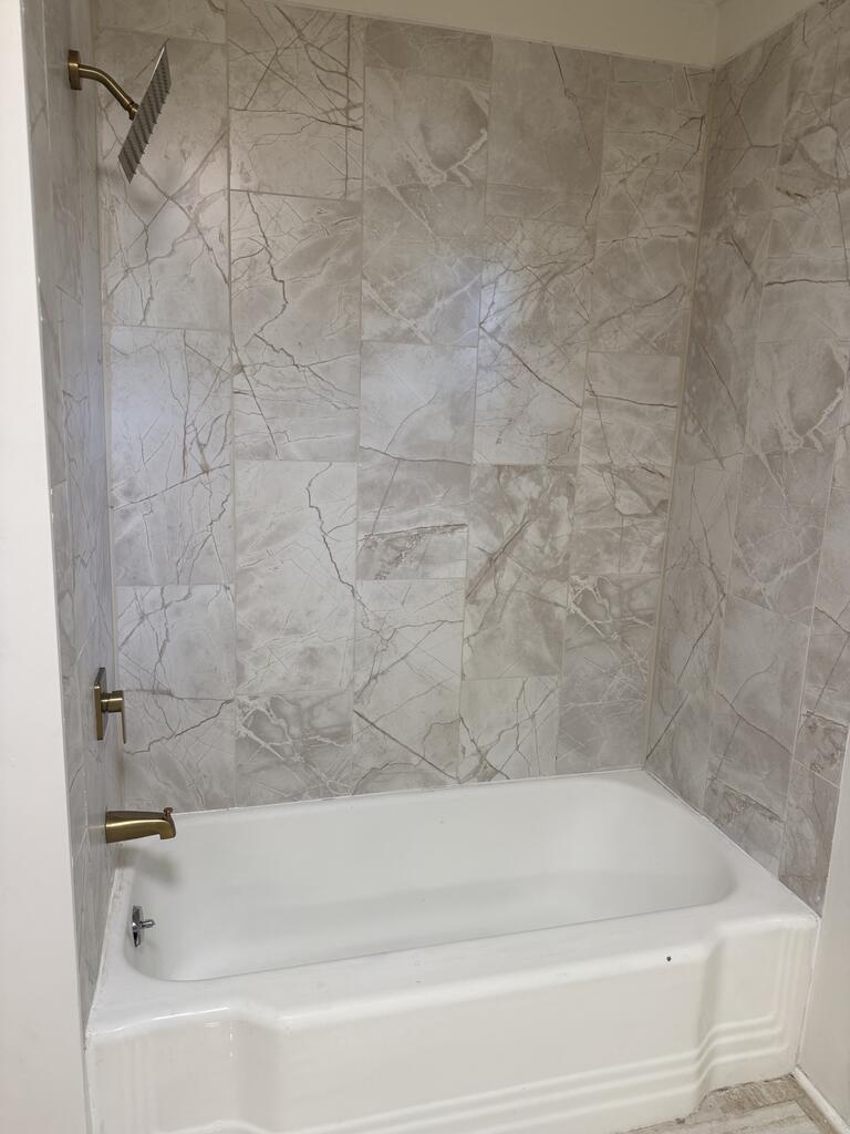 Bathroom tub and shower with gray marble-look tile and brass-colored fixtures.
