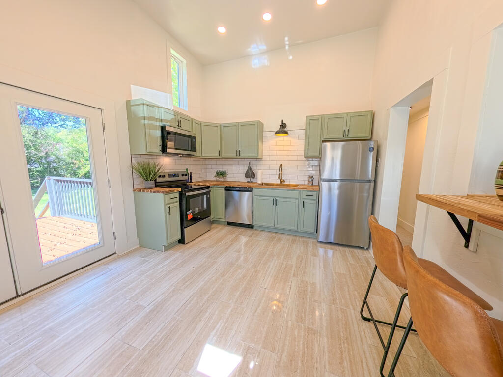 Kitchen with sage-green cabinets, stainless steel appliances, and a glass door to the deck.