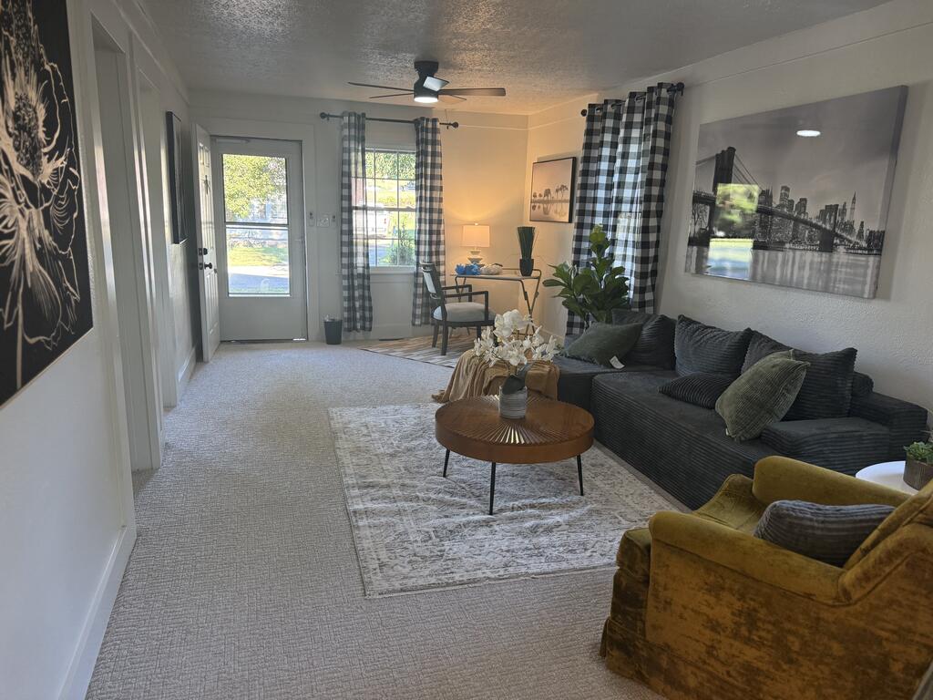 Living room with a dark sectional, mustard armchair, and glass-panel entry door beside curtained windows.