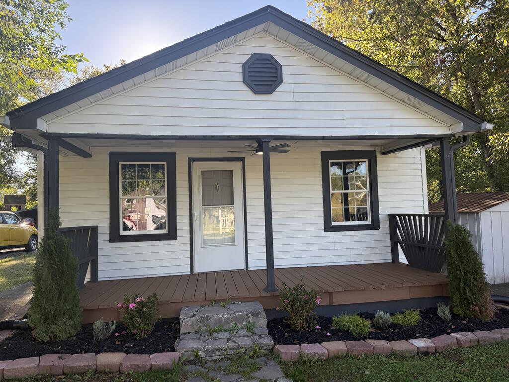 White single-story home with dark trim, a front gable, and a raised wooden porch.