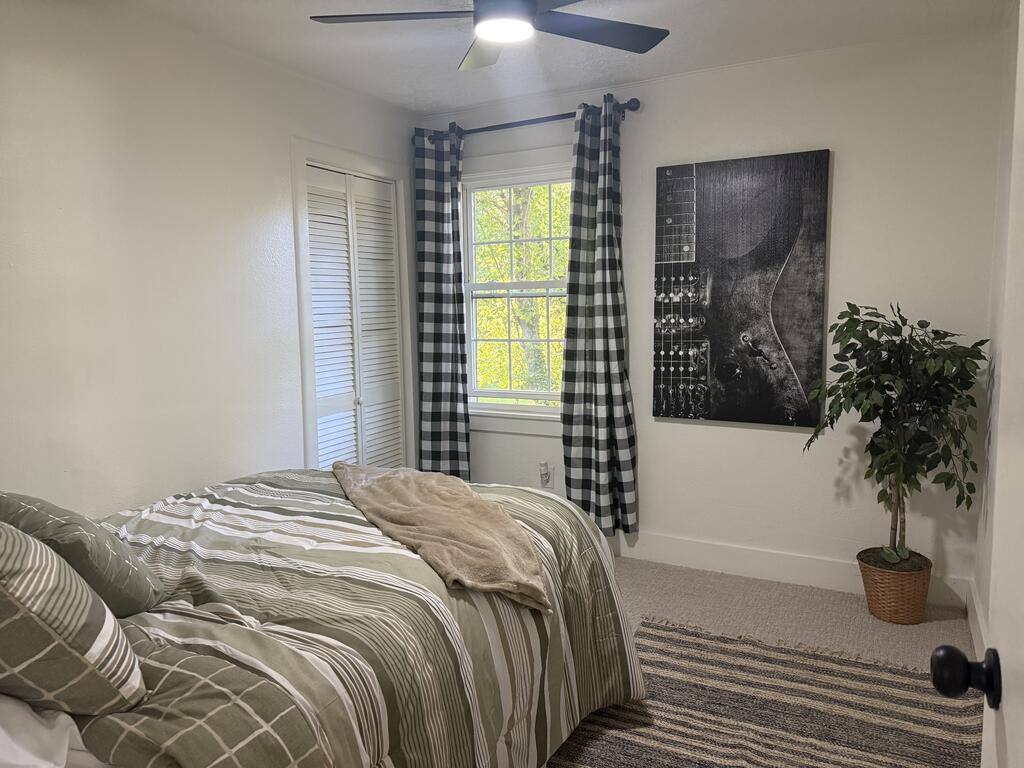 Bedroom with green striped bedding, checkered curtains, and a sunlit window.