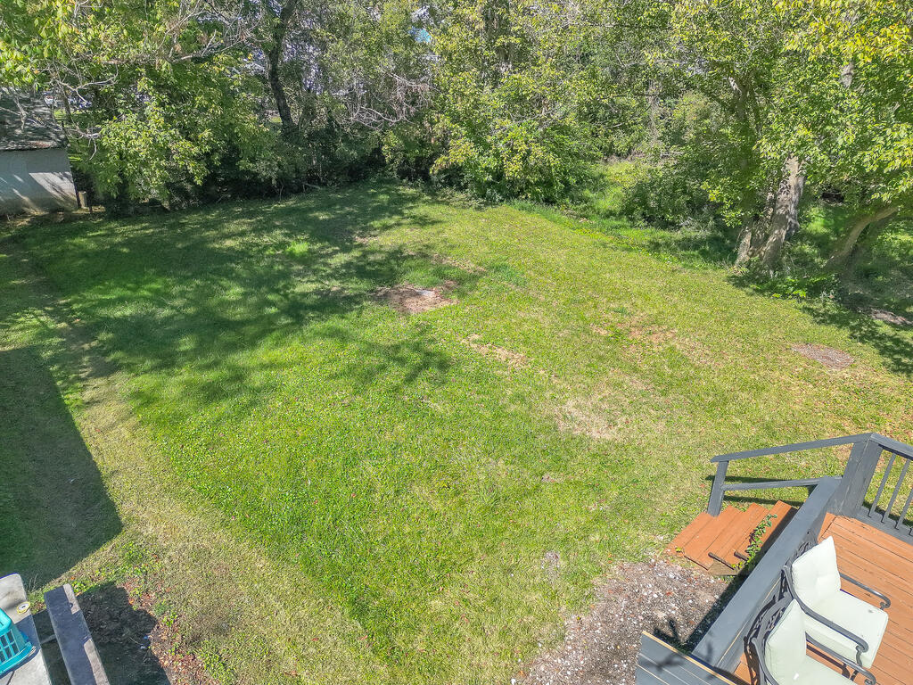 Grassy backyard bordered by mature trees, viewed from a deck with white patio seating.