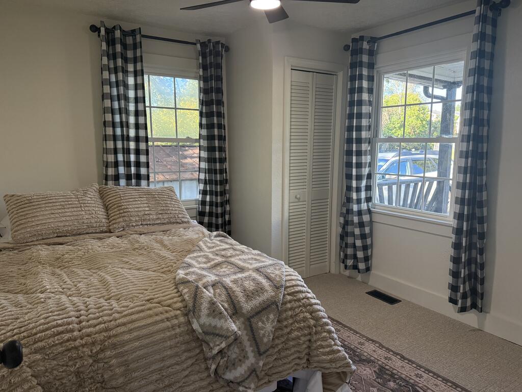 Bedroom with a beige textured bedspread and checked curtains framing two windows.