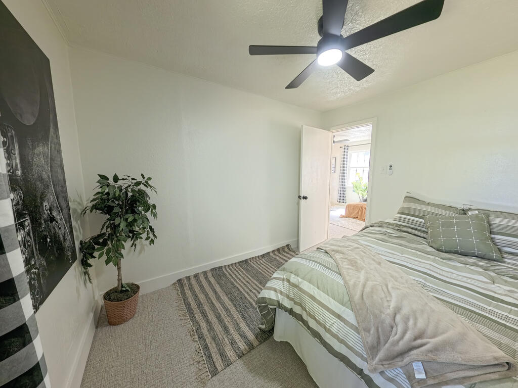 Staged bedroom with striped bedding, a ceiling fan, and a potted plant beside an open doorway.