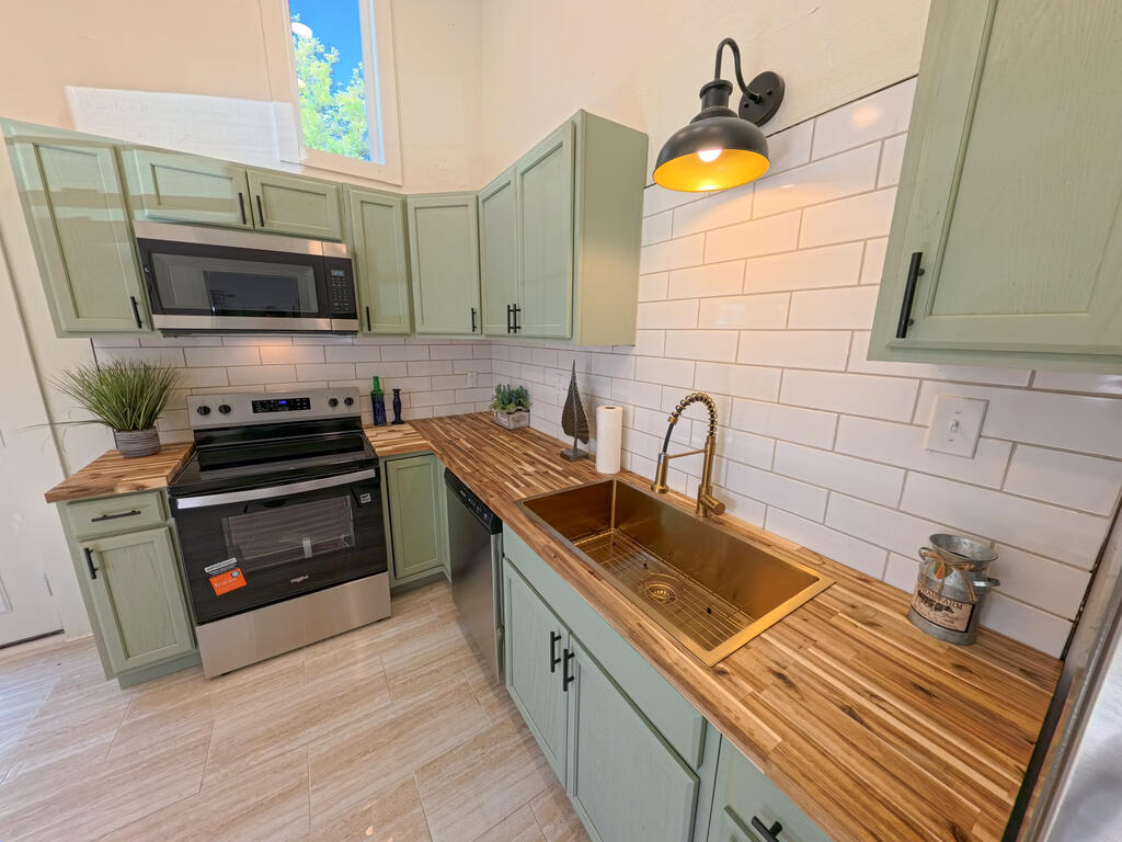 Kitchen with sage-green cabinets, butcher-block counters, white subway tile, and a copper-toned farmhouse sink.