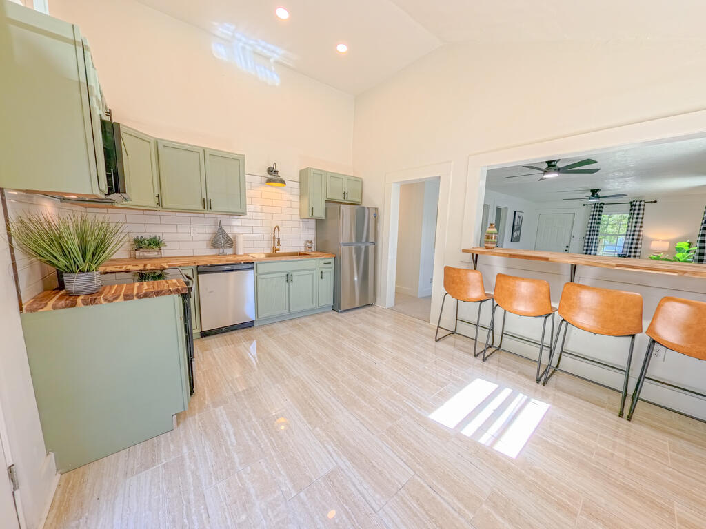 Kitchen with sage-green cabinets, marble-pattern counters, and orange stools at the breakfast bar.