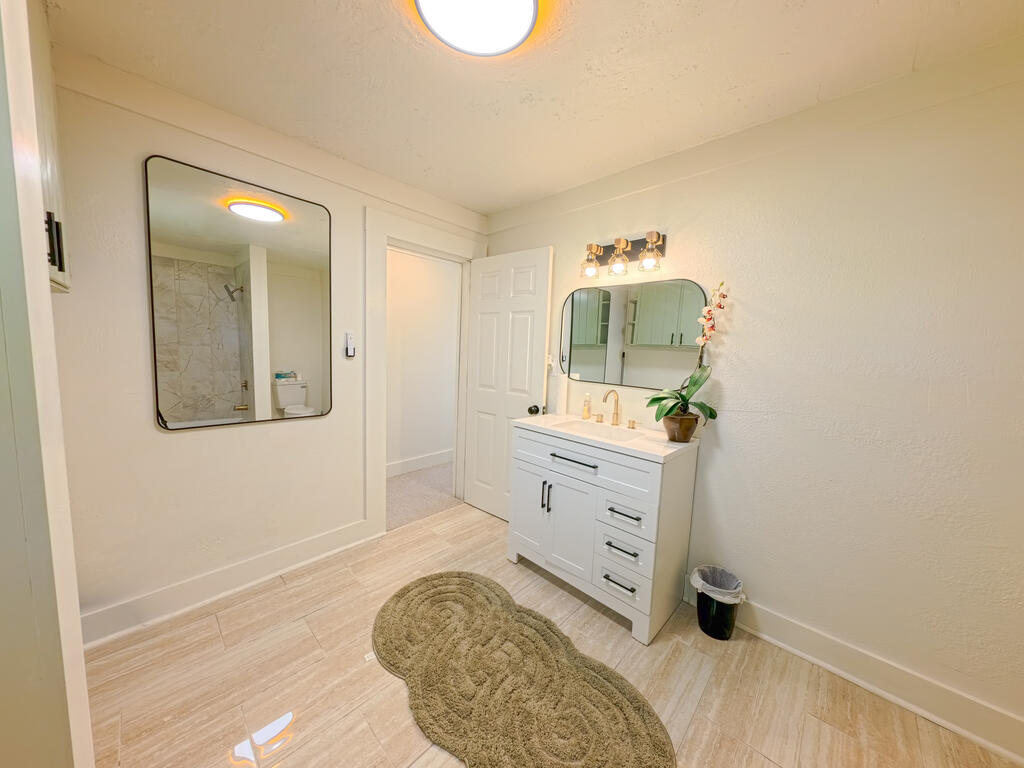 Bathroom with a white vanity, mirrored cabinet, and woven tan rug on light tile.