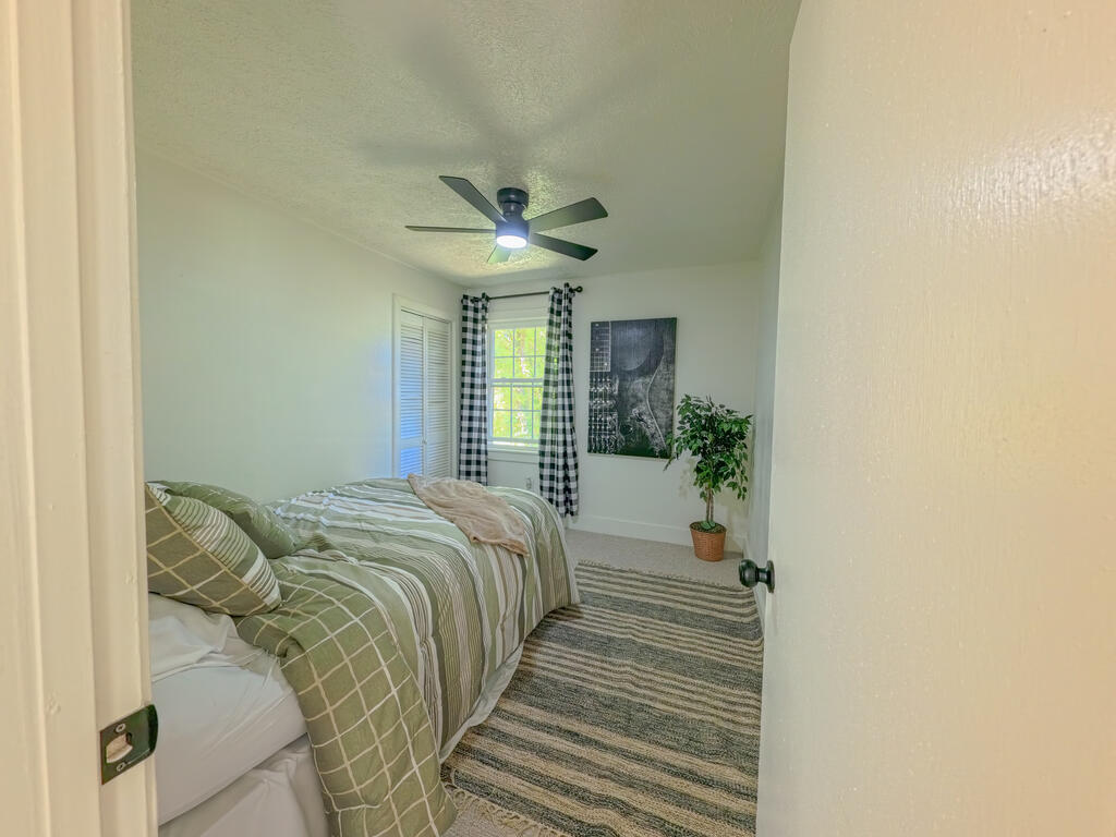 Furnished bedroom with green striped bedding, checked curtains, a ceiling fan, and a striped rug.
