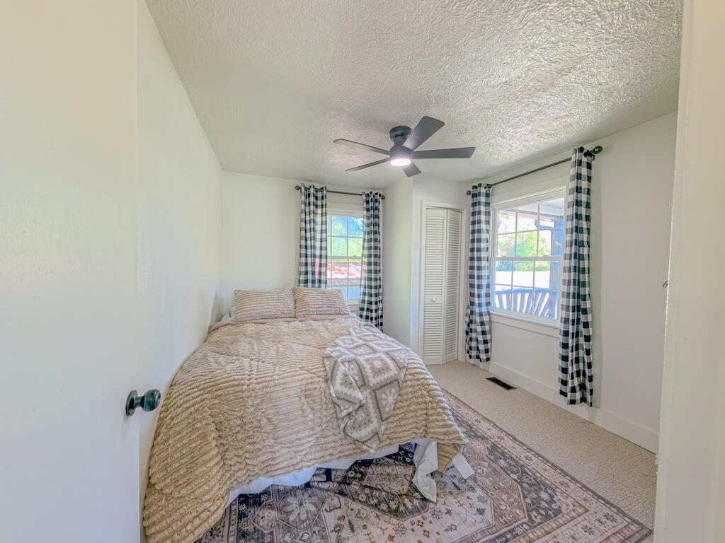 Furnished bedroom with beige bedding, checked curtains, and a ceiling fan.