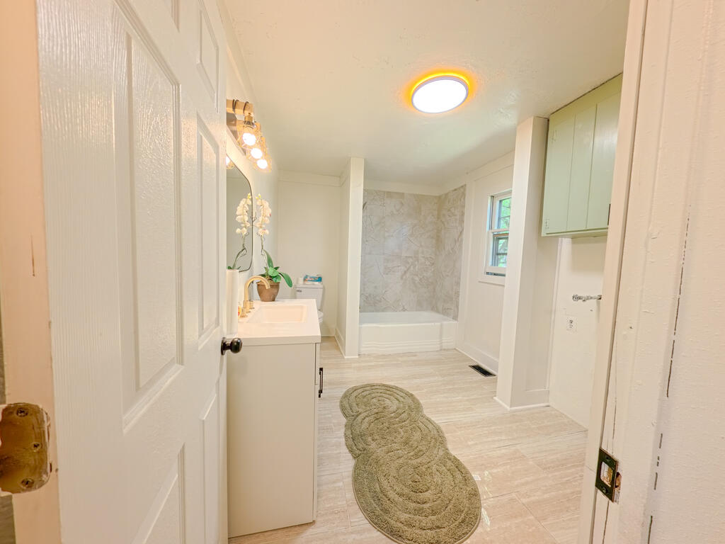 Bathroom with a marble-pattern tub surround, pale green cabinets, and a white vanity with an orchid.