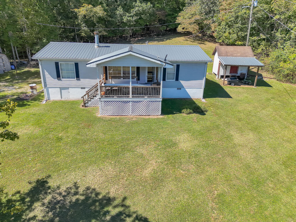 Light-blue home with a covered front porch and metal roof, viewed from above with a detached carport nearby.