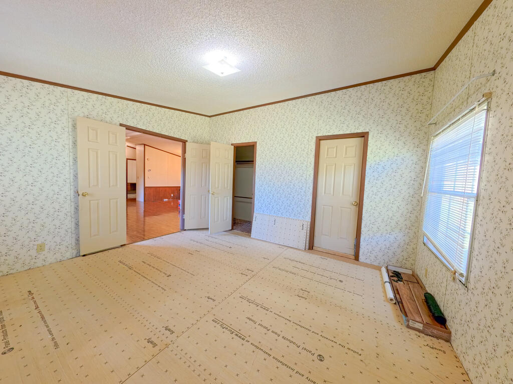 Unfinished bedroom with patterned wallpaper, exposed subfloor, an open closet, and a window with blinds.