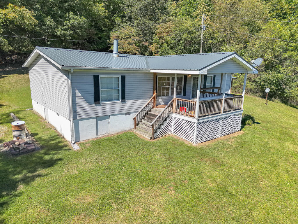 Gray single-story home with a metal roof and raised wooden front porch, surrounded by lawn and trees.