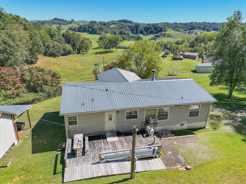 Rural home with a gray metal roof and wooden deck, surrounded by green fields and distant rolling hills.