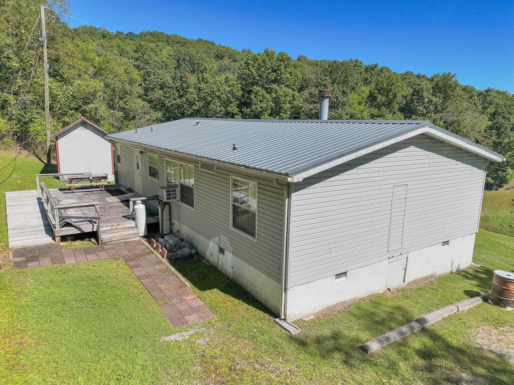 House with a gray metal roof, wooden deck, and detached shed beside a wooded hillside.