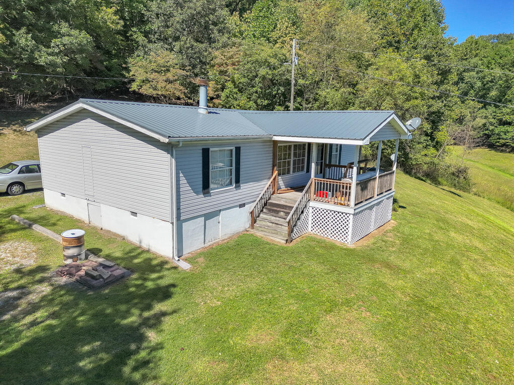 Gray single-story home with a metal roof and covered porch, surrounded by lawn and trees.