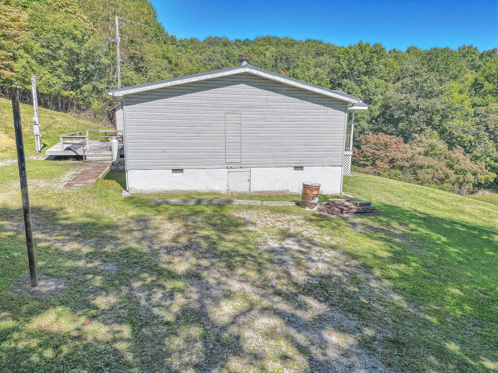 Gray-sided home with a broad gable end, small deck, and sloping tree-lined yard.
