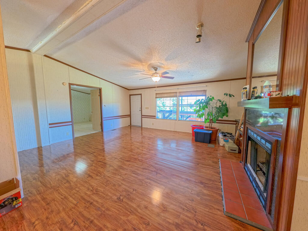 Mostly empty living room with glossy wood-pattern floors, a tiled fireplace, and large windows overlooking a deck.