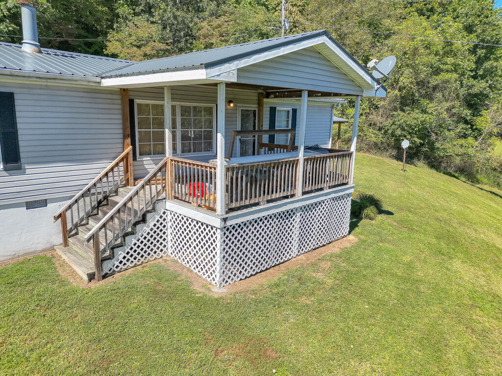 Light-blue home with a covered porch, wooden steps, white lattice skirting, and a tree-lined lawn.
