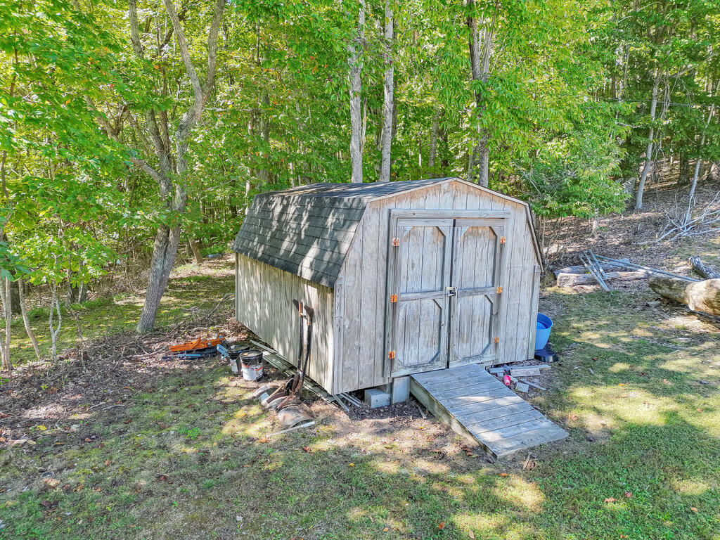 Weathered wooden storage shed with double doors and a ramp in a wooded yard.