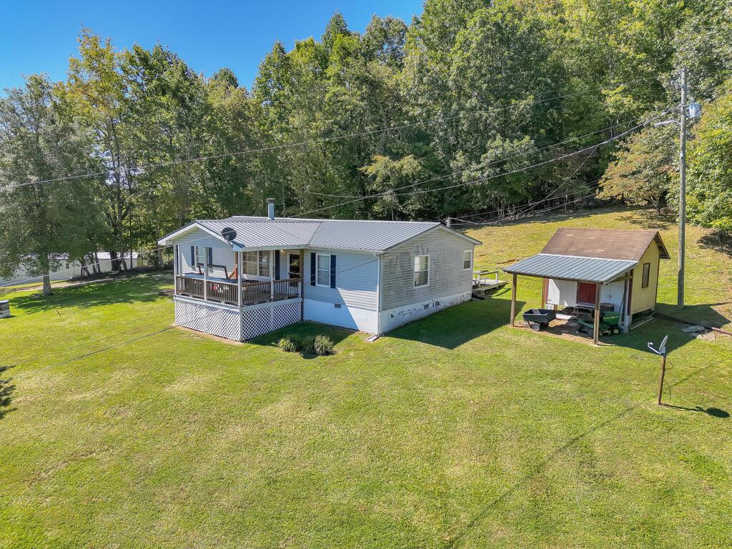 Light-blue single-story home with a covered porch and small outbuilding on a large grassy lot.