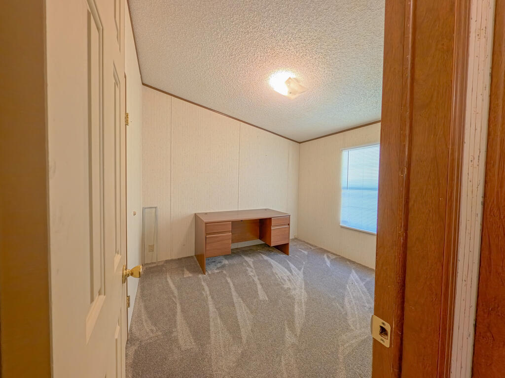 Carpeted room with a wooden desk against the wall and a window with closed blinds.