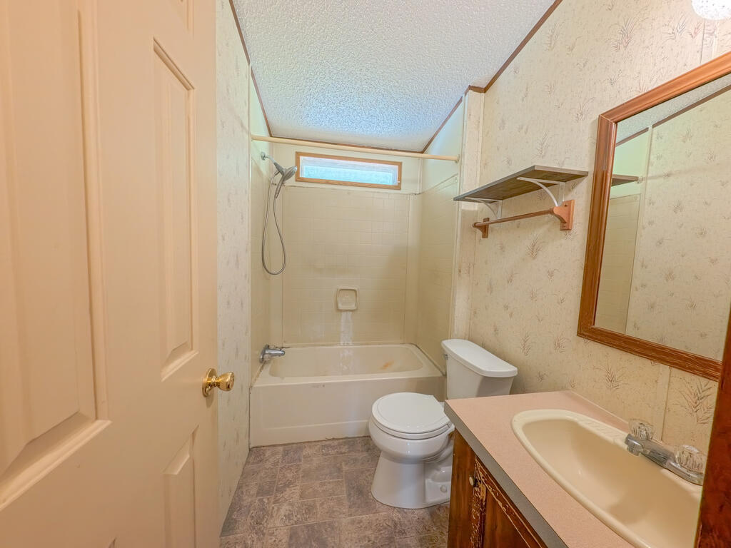 Bathroom with a bathtub and shower, toilet, and sink vanity beneath a wood-framed mirror.