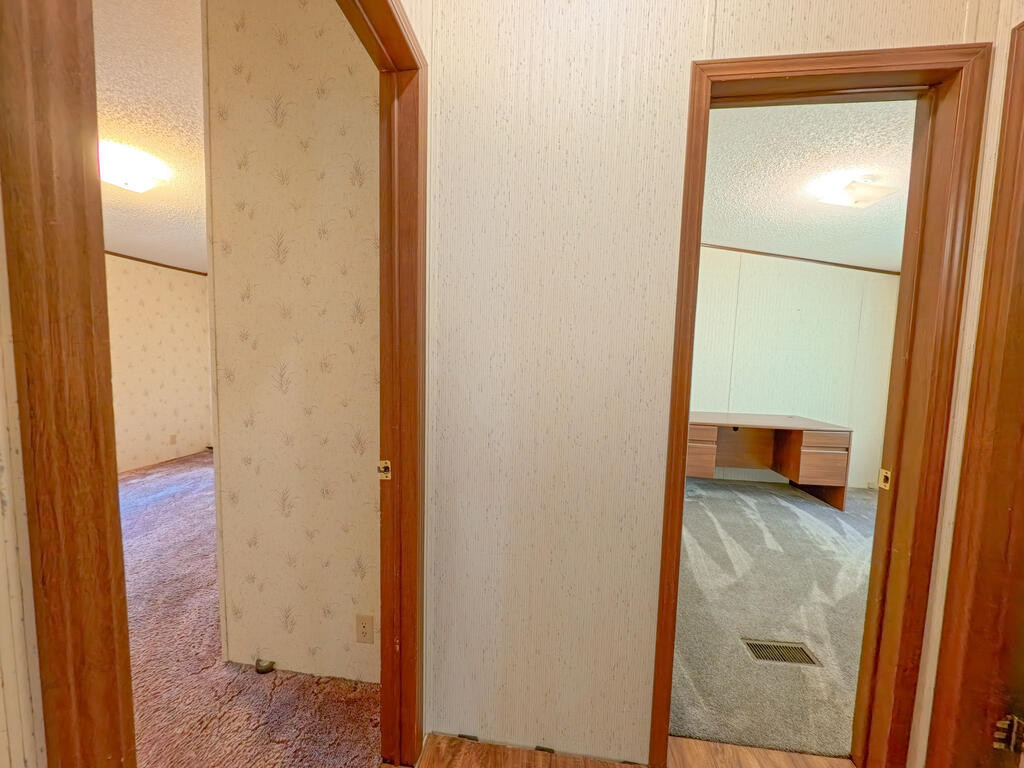 Hallway with patterned wallpaper and wood-trimmed doorways opening to carpeted rooms.