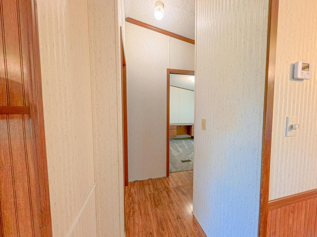 Hallway with wood-look flooring and an open doorway to a carpeted room with built-in cabinetry.