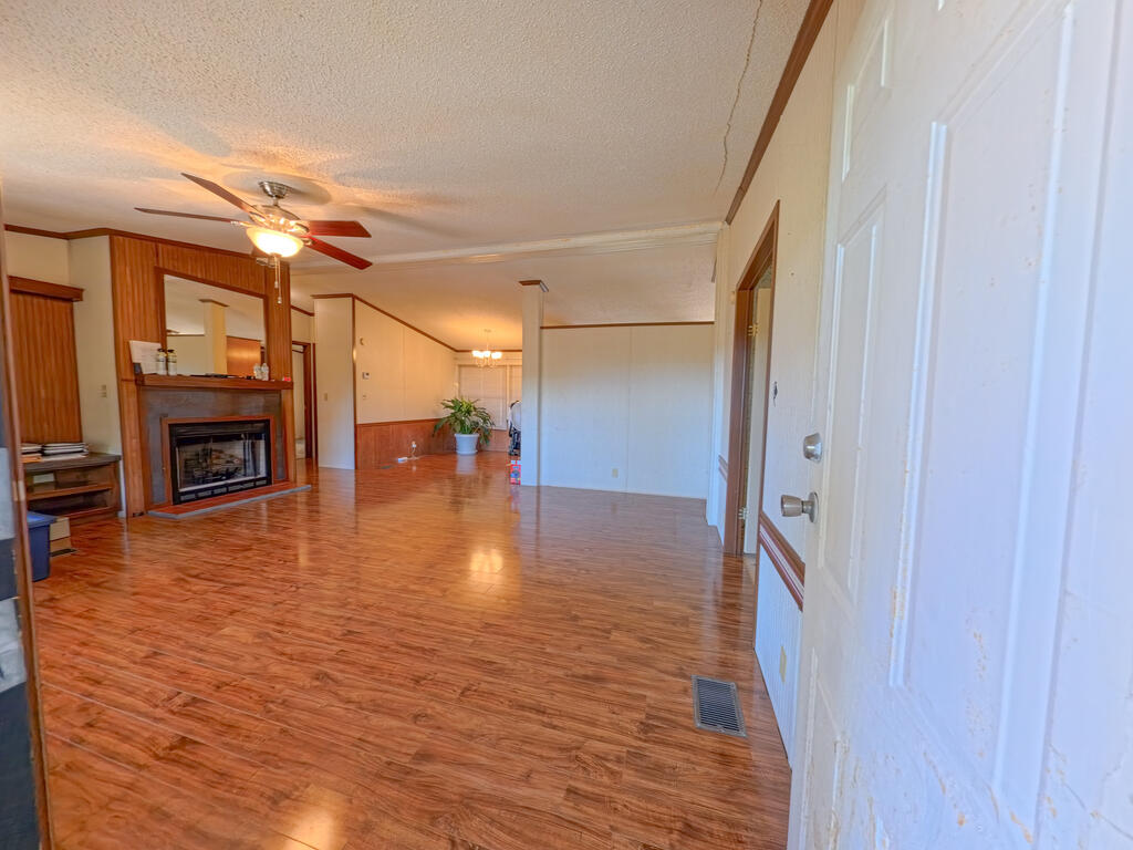 Living room with glossy wood-look flooring, a wood-trimmed fireplace, and a ceiling fan.