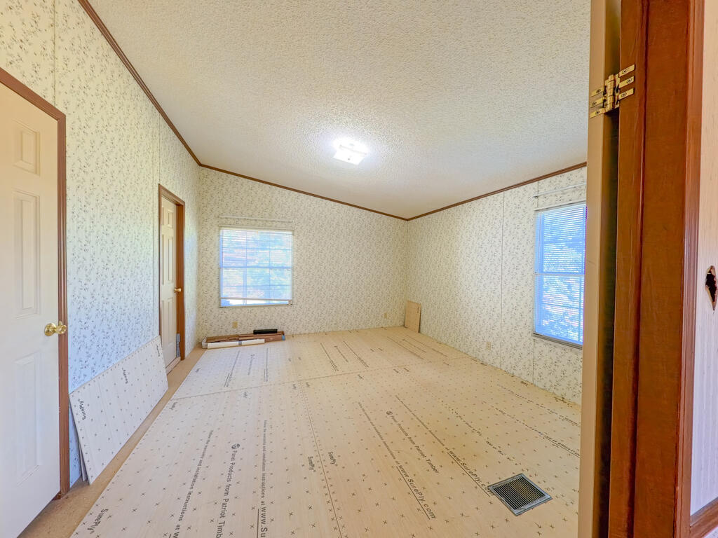 Empty room under construction with unfinished flooring, patterned wallpaper, and two windows.