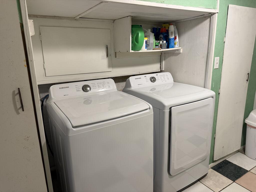 Laundry room with matching white Samsung washer and dryer beneath cabinets stocked with cleaning supplies.