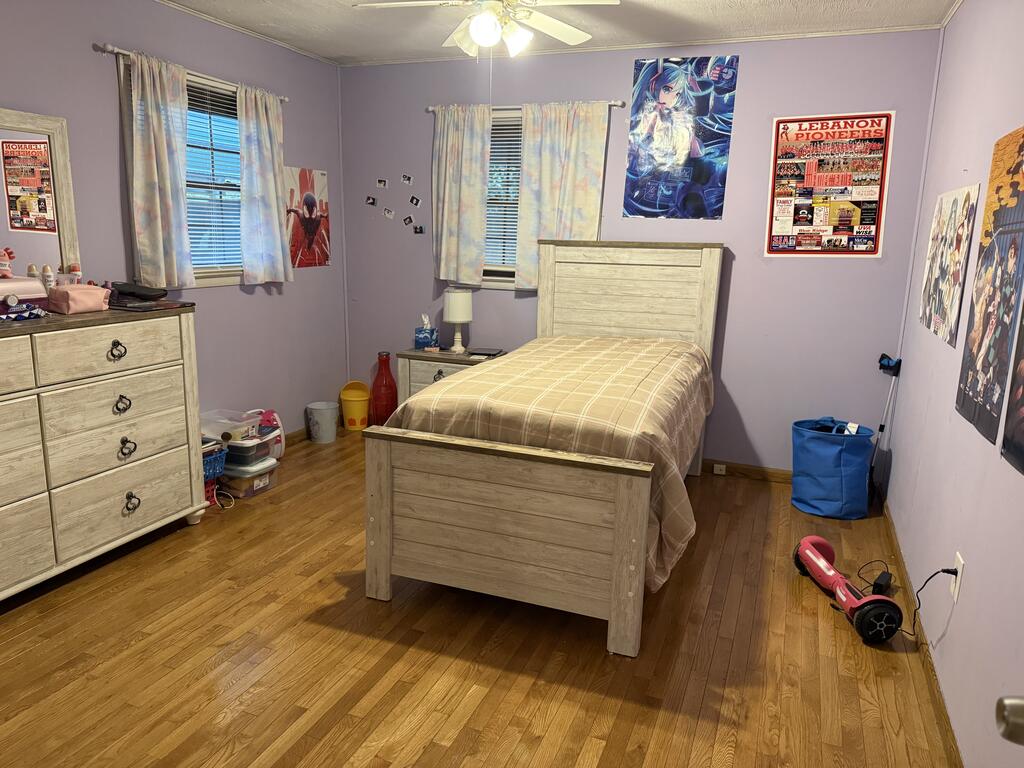 Bedroom with lavender walls, hardwood floors, and light wood furniture beneath colorful wall posters.