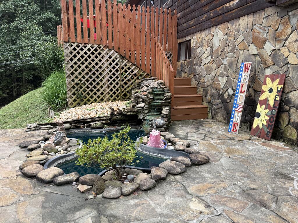 Stone patio with a small rock-edged pond beside a stone-sided home and wooden steps.