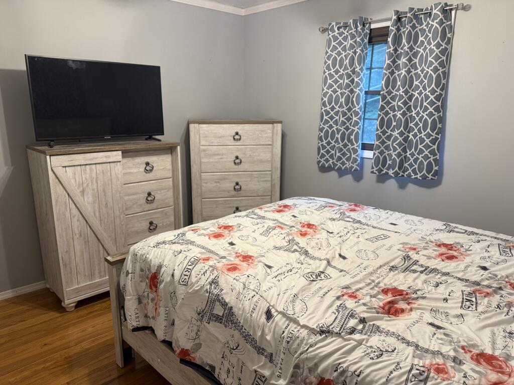 Bedroom with rose-print Paris bedding, light wood dressers, a television, and patterned curtains.