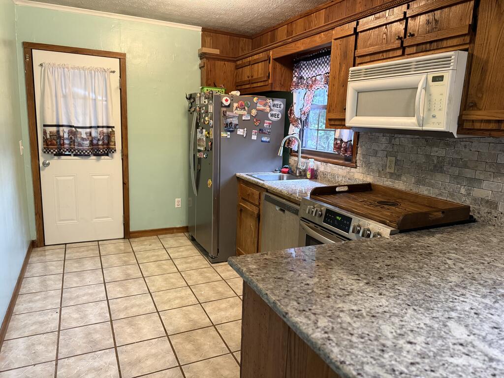Kitchen with wood cabinets, granite counters, gray tile backsplash, and a refrigerator covered in magnets.