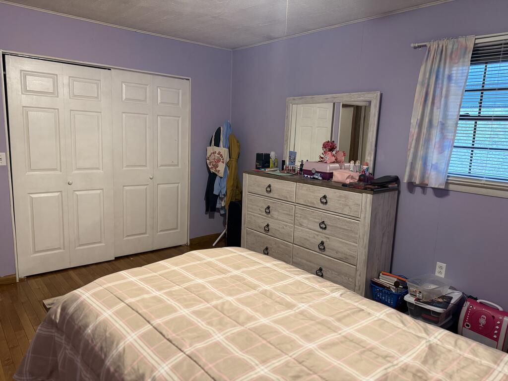 Furnished bedroom with lavender walls, white closet doors, and a wood dresser with mirror.