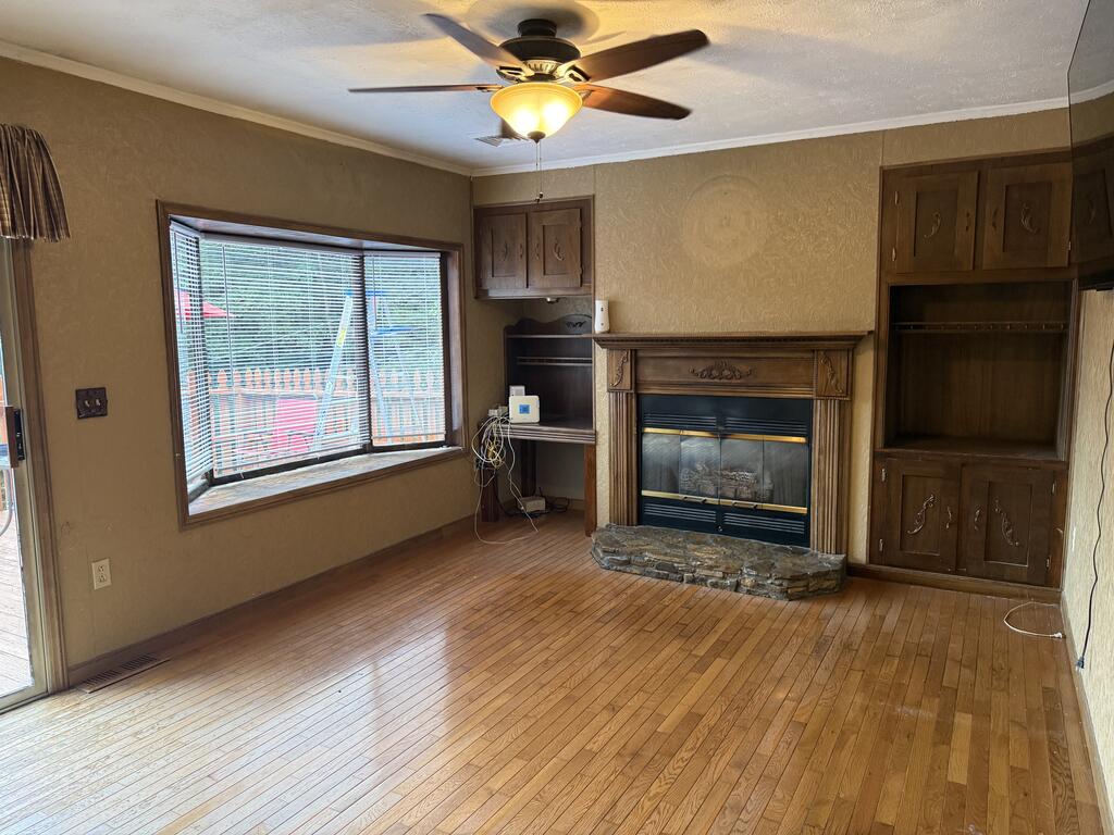 Living room with hardwood floors, a wood-trimmed fireplace, built-in cabinets, and a large window.