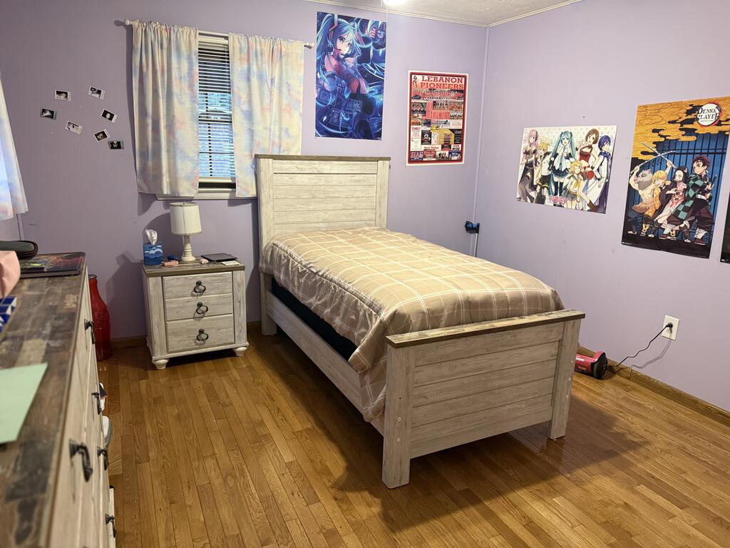 Bedroom with a light wood single bed, lavender walls, hardwood floors, and anime posters.