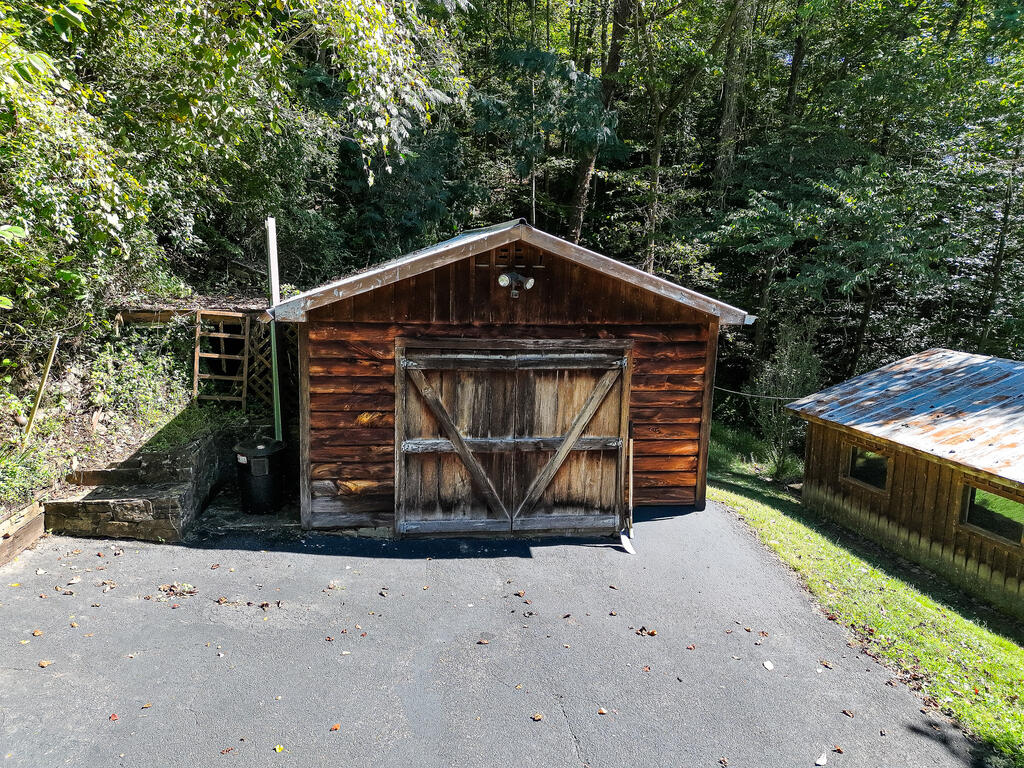 Detached wooden garage with weathered double doors beside a wooded driveway.