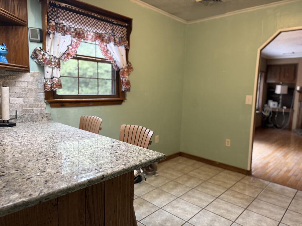 Kitchen with a granite peninsula, wood cabinets, and a window framed by floral curtains.