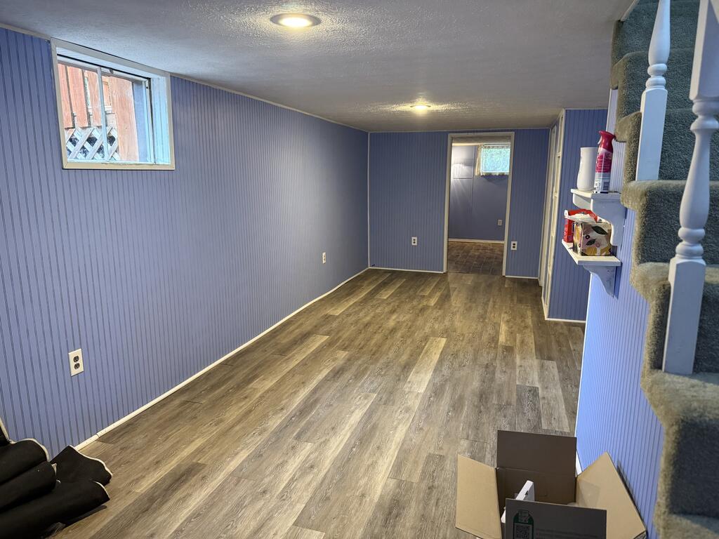 Finished room with blue paneled walls, wood-look flooring, a small window, and carpeted stairs.