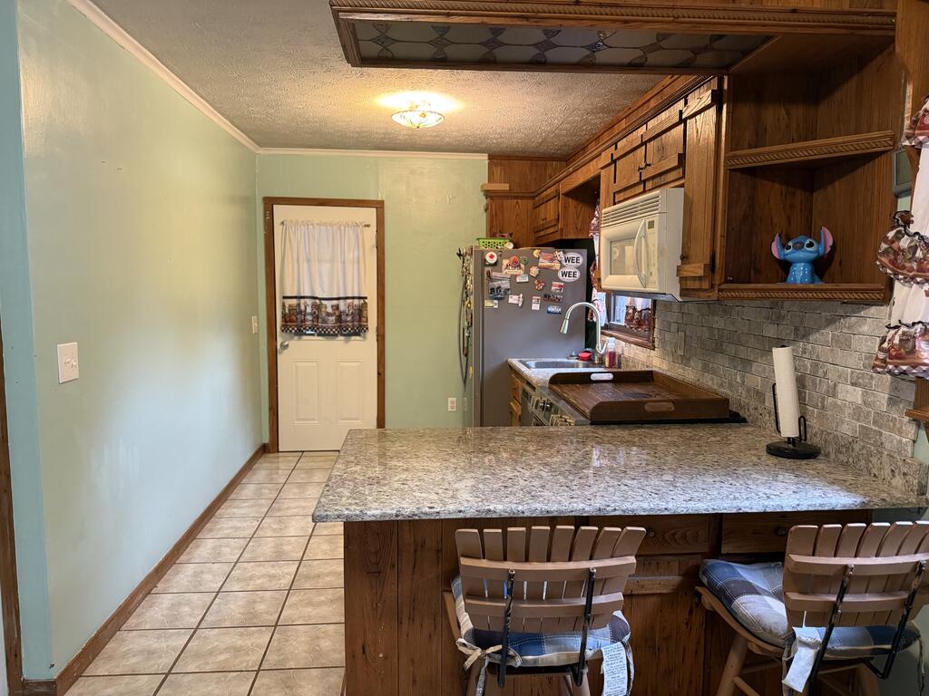 Kitchen with dark wood cabinets, stone-tile backsplash, and a granite breakfast bar with two chairs.