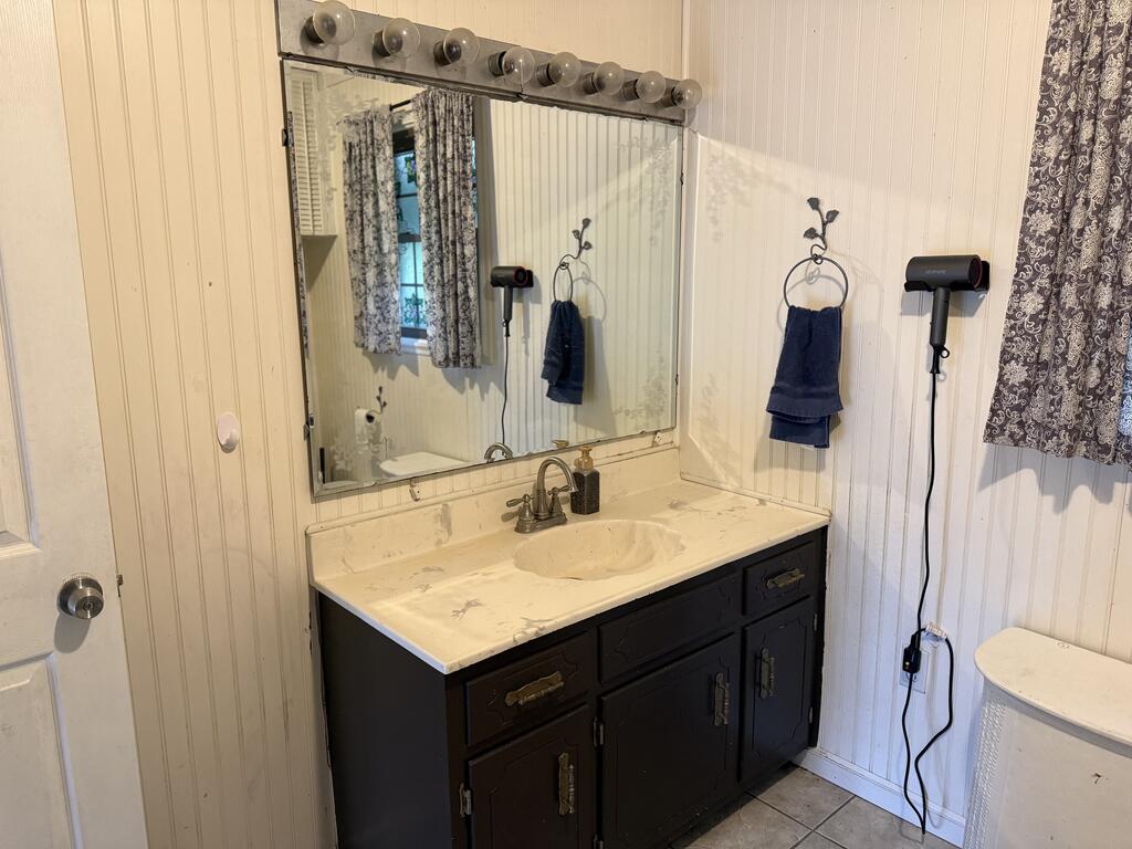 Bathroom vanity with a cream sink counter, dark cabinets, and a large mirror.