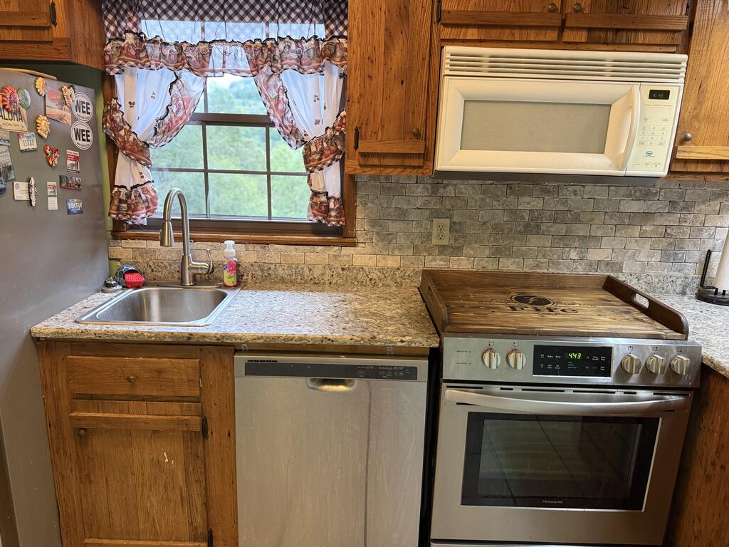 Kitchen with wood cabinetry, stainless steel appliances, patterned backsplash, and a window above the sink.