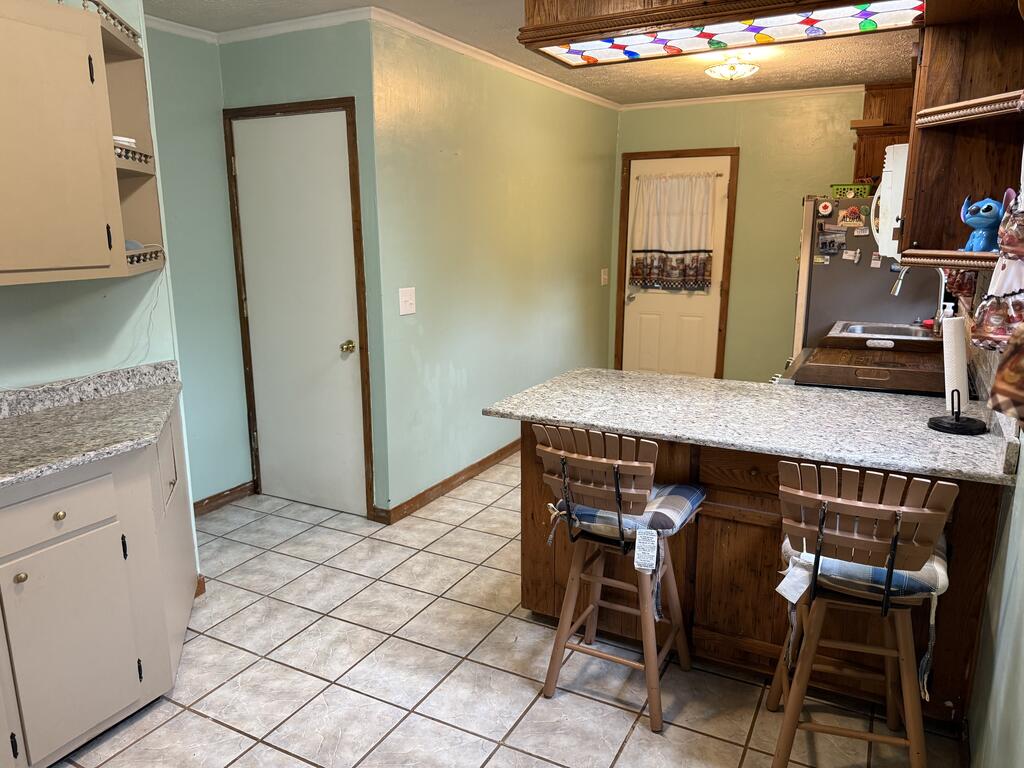 Kitchen with granite island, wood cabinetry, tiled floor, and colorful stained-glass ceiling light.